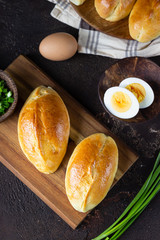Fresh baked pasties filled with green onion and egg on a wooden cutting board, dark concrete background. Russian pirozhki. Top view.