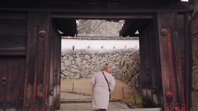 Female Tourist Walking Through The Entrance Door Of Himeji Castle In Japan In Slow Motion - tilt down shot