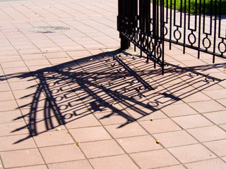Metal gate and fence and its shadow on the pavement