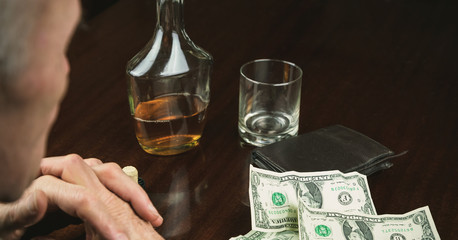 retired man sits at brown wooden table near banknotes by wallet and alcohol in bottle