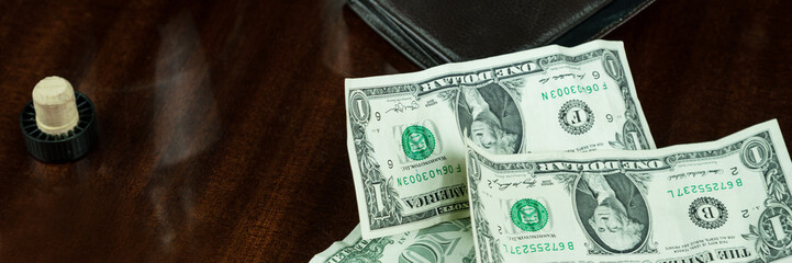 dollar banknotes lie near black wallet and cognac bottle with glass on brown wooden table