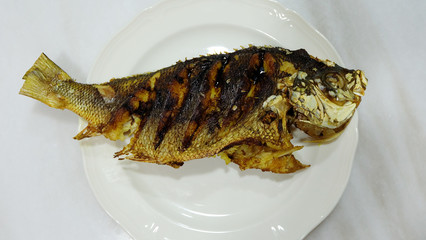 A whole fusilier fish, fried and served on a plate. Top view.