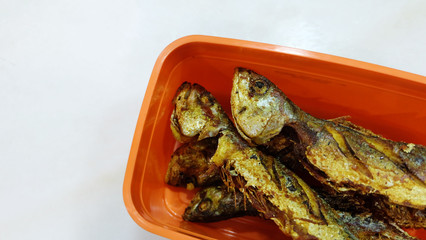 Fried shrimp scad fishes in a red plastic container, on a marble surface.