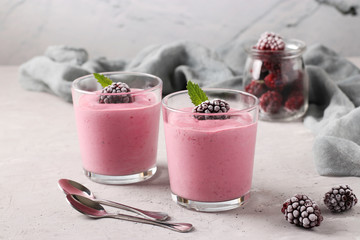Two servings of homemade smoothies with frozen blackberries in glasses on gray concrete background, Diet and weight loss control concept, Closeup