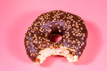 Bitten donut with chocolate glaze on top isolated on a pink background