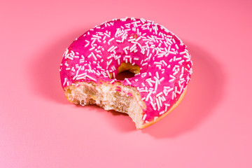 Bitten donut with glazed top isolated on a pink background