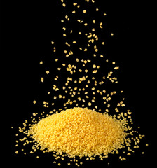 Falling dry couscous groats isolated on black background