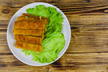 Baked fish sticks and lettuce leaves in a plate. Top view