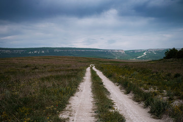 Fototapeta premium Dirt road among the spring field. Before the storm