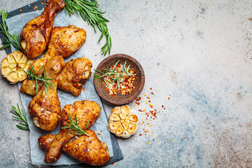 Baked spicy chicken legs with rosemary and garlic on black slate, dark background, top view.