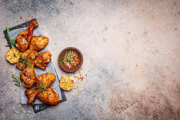 Baked spicy chicken legs with rosemary and garlic on black slate, dark background, top view.