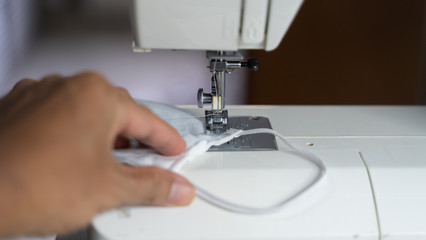 Electric sewing machine with fabric and thread, defocus hand hold on protective mask , antivirus  face mask during a pandemic virus COVID-19