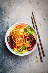 Vegetable noodles - zucchini, beets and carrots in white bowl, dark background. Raw vegan food.