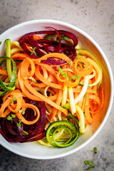 Vegetable noodles - zucchini, beets and carrots in white bowl, dark background. Raw vegan food.
