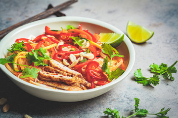 Pad thai noodles with chicken, peanuts and vegetables in bowl, dark background.