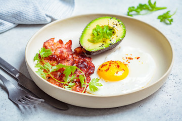 Keto breakfast - fried egg, avocado and fried bacon in white plate. Keto diet concept.