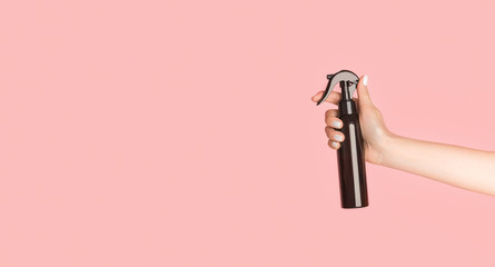 Unrecognizable lady holding sprayer bottle with cosmetic oil, lotion or sunscreen on pink...