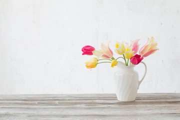 beautiful tulips in white jug on wooden background