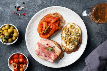 Wholegrain bread sandwiches with cream cheese, bacon and olives canned peppers with tomato on a plate. Dark concrete background with Copy space.