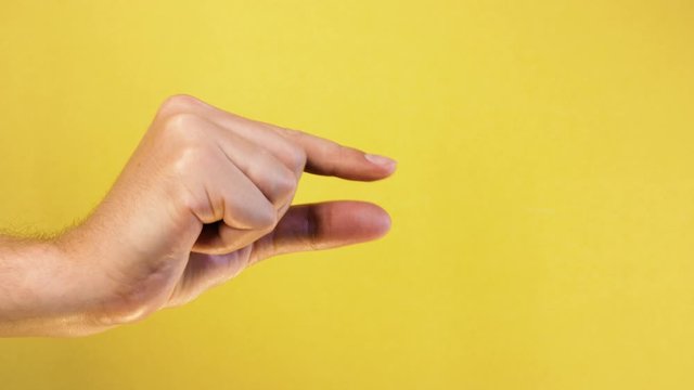 Man caucasian hand showing gesture of little size with two fingers, isolated over yellow background. Showing small thing gesture