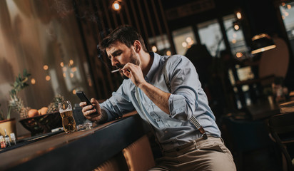 Man drinking beer, smoking cigarette and using mobile phone at pub