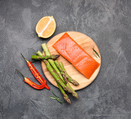 Asparagus with salmon, lemon and chili pepper on dark background