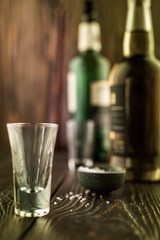 An empty tequila glass in front of many colorful liquor bottles, shallow depth of field, selective focus.