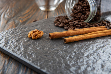 Anise stars and cinnamon sticks on a stone tile, go for the grains of coffee that get enough sleep from a glass jar, in the background an empty glass cup. Coffee seasoning concept.
