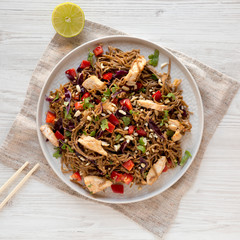 Homemade Spicy Chicken Soba Noodle Salad on a gray plate on a white wooden table, overhead view. Flat lay, from above, top view.