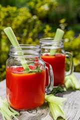 Two glasses of tomato juice with parsley and celery decorations, stand in the open air on wooden boards, the rays of the sun shine, shallow depth of field, selective focus. The concept of natural