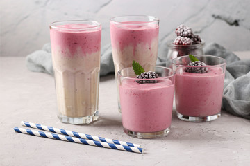 Four servings of homemade protein cocktail with frozen blackberries, banana and yogurt in glasses on gray concrete background, Diet and weight loss control conceptm Closeup