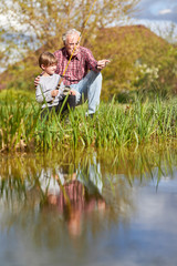 Fototapeta premium Opa zeigt seinem Enkelsohn das Angeln am See