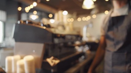 Selective focus of male waiter in black apron giving coffee in takeaway cup to customer