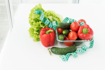 big transparent plate with measuring tape and vegetables: salad, tomatoes, bell peper, zucchini, cucumber.  dieting concept. way of loosing weight and calories control, healthy eating and lifestyle.