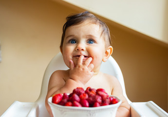 Baby infant toddler sit in highchair, eat first supplementary vegan food - strawberry. 