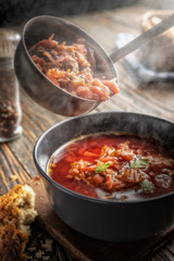 Tomato soup with vegetables and meat is poured into a bowl from the ladle from which steam comes, tasty, appetizing traditional Ukrainian borsch, close-up, shallow depth of field, selective focus