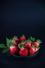 Fresh juicy strawberries in a black plate on a black matte background