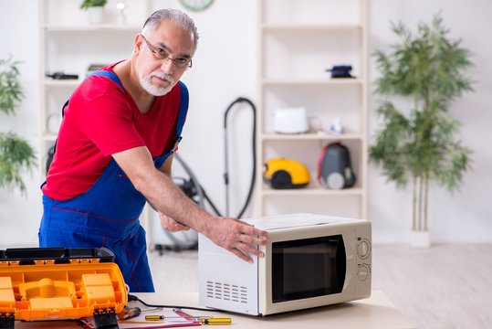 Old Male Contractor Repairing Microwave Indoors