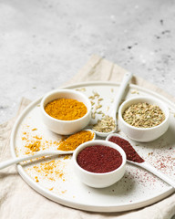 Spices and condiments in white bowls on a light gray table. Turmeric, ginger, curry, fennel and sumac in white bowls. Spices close up