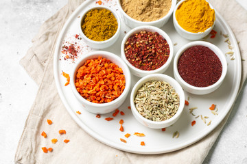 Spices and condiments in white bowls on a light gray table. Turmeric, ginger, curry, fennel and sumac in white bowls. Spices close up