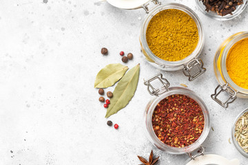 Spices and condiments in glass jars on a light gray table. Spices close-up with space for text. The view from the top