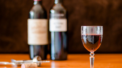 A GLASS OF WINE WITH SEVERAL BOTTLES OF WINE IN THE BACKGROUND 