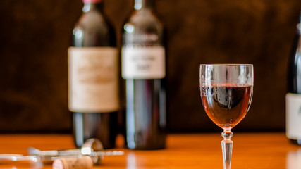 A GLASS OF WINE WITH SEVERAL BOTTLES OF WINE IN THE BACKGROUND 