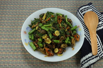 Fried spicy fresh mussel meats with chilly, cutting green bean, chopped fresh baby corn and basil on the plate. Famous comfortable seafood menu in Asia. Hot plate in street food. 