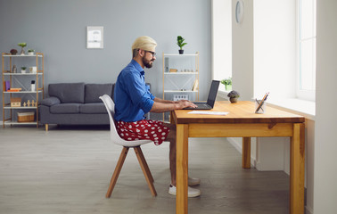 Online work at home. A young man in typing in a laptop sitting at a table at home. Remote work.