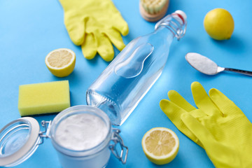 natural cleaning stuff and eco living concept - bottle of vinegar, lemons, rubber gloves, washing soda with sponge and brush on blue background