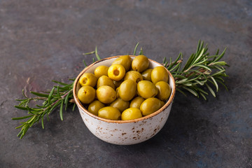 Green olives in a bowl with rosemary on dark background.