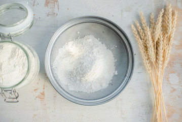 A flour in the sieve and wheat stems on the white kitchen table flat lay background.