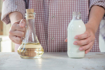 Woman is holding a fresh milk in the bottle and sunflower oil close up.
