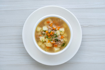 Fresh fish soup with carrots, potatoes and onions in a white plate, close up. Tasty dinner consists of a fish soup with tuna